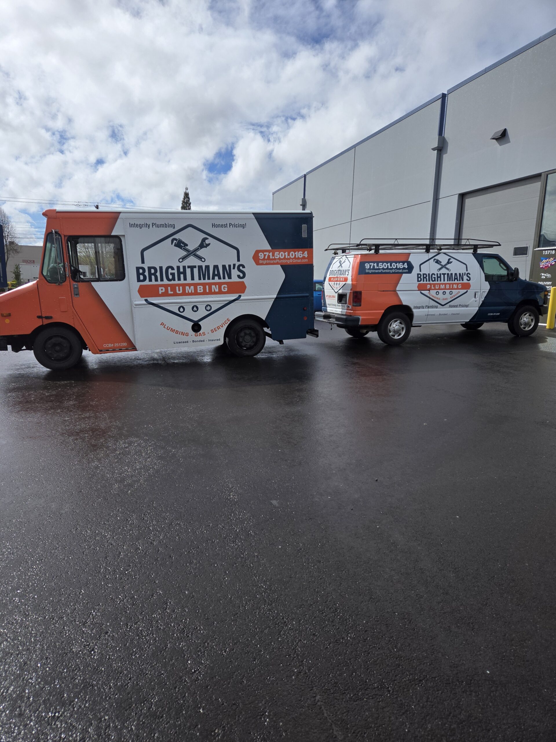 Two Brightman's Plumbing service vehicles parked outside a commercial building on a wet asphalt lot under a cloudy sky.
