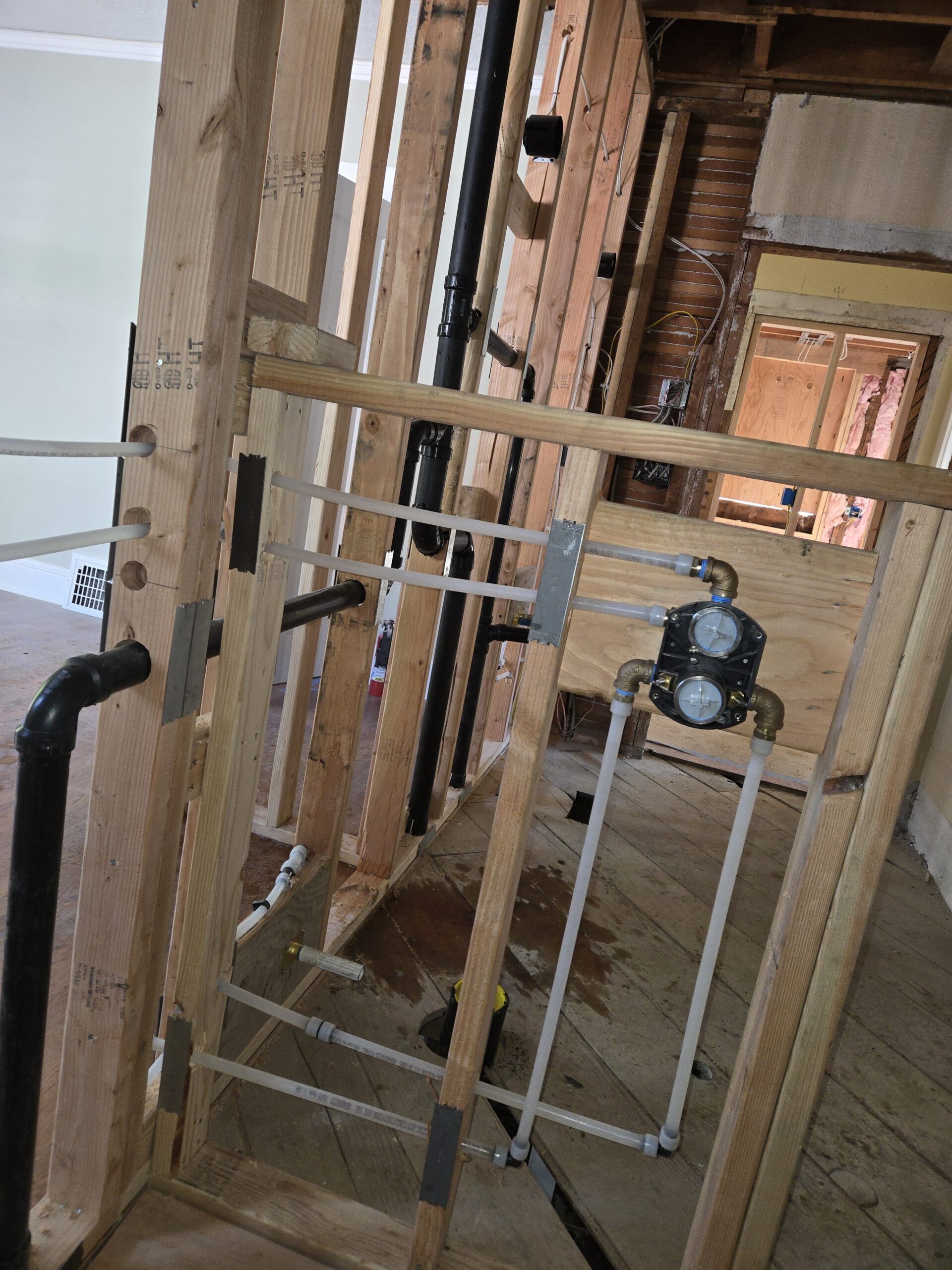 Unfinished bathroom construction with exposed wooden studs, plumbing pipes, and a shower valve partially installed in the wall.